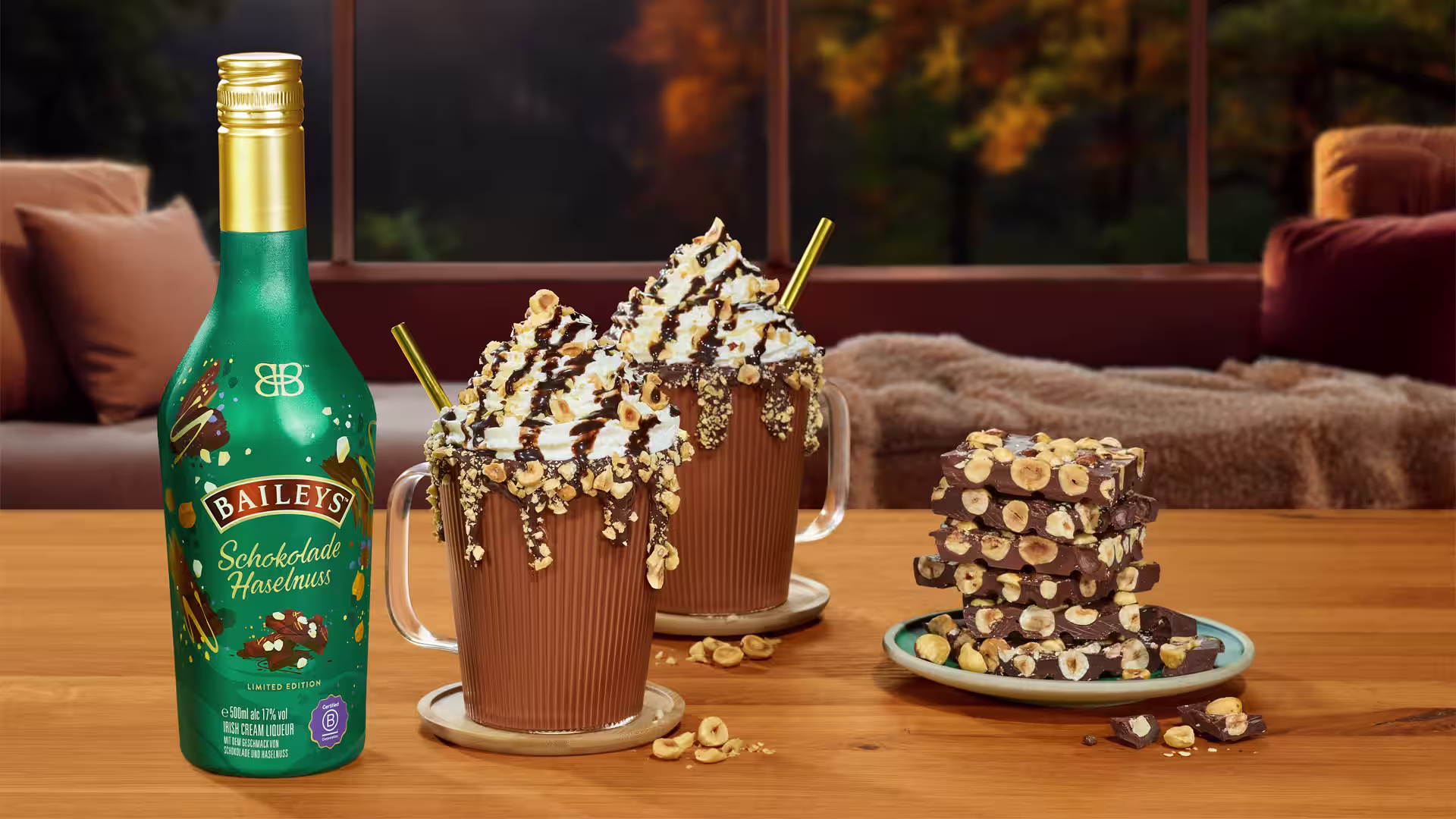 Baileys Schokolade Haselnuss bottle with two whipped cream hot chocolates, topped with hazelnuts and chocolate drizzle.