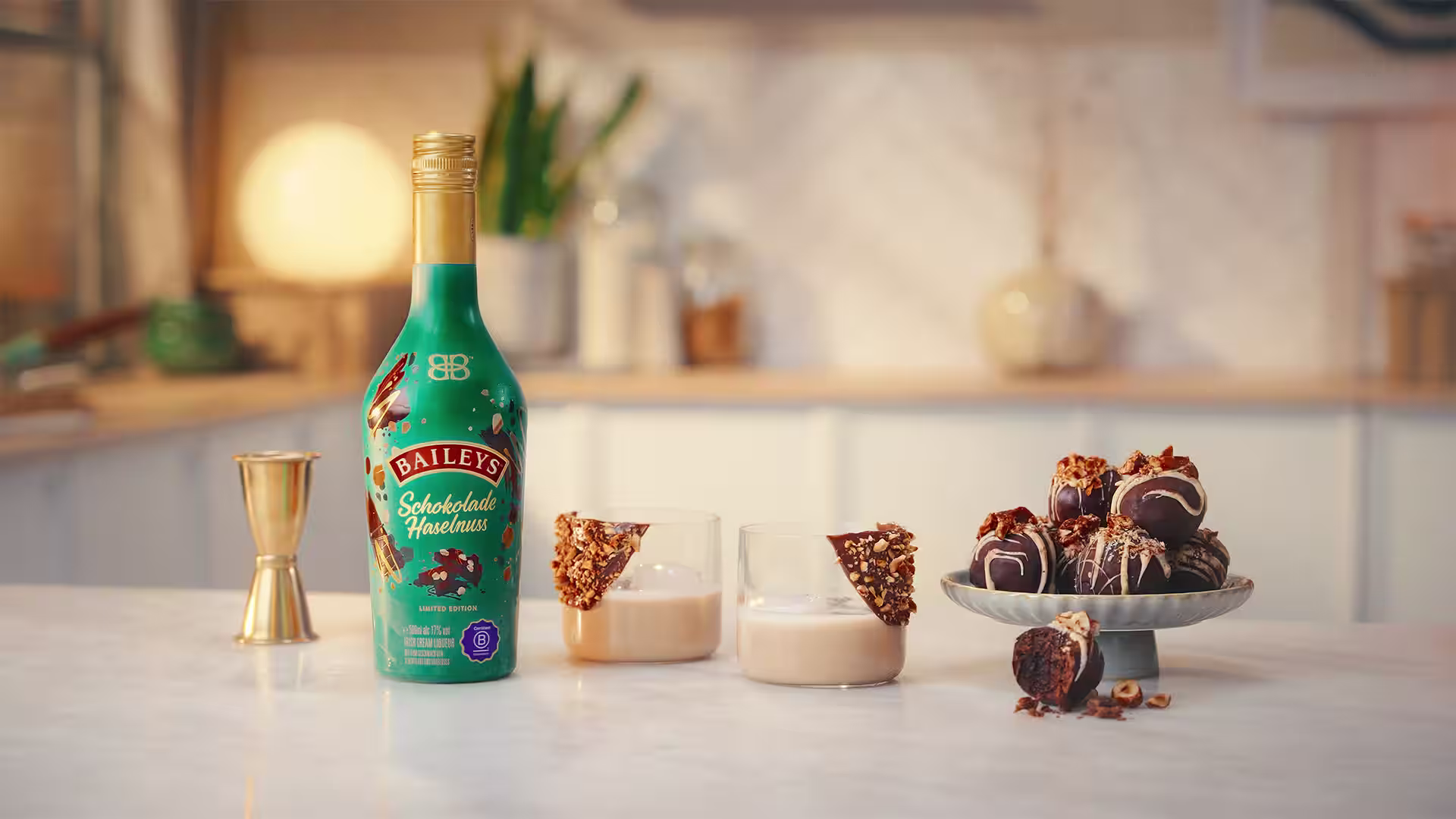 Baileys Schokolade Haselnuss bottle with two short serves and hazelnut chocolate truffles on a stand.