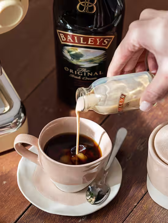 Baileys Irish Cream being poured into a steaming cup of black coffee, creating a swirling blend of creamy and dark coffee tones.