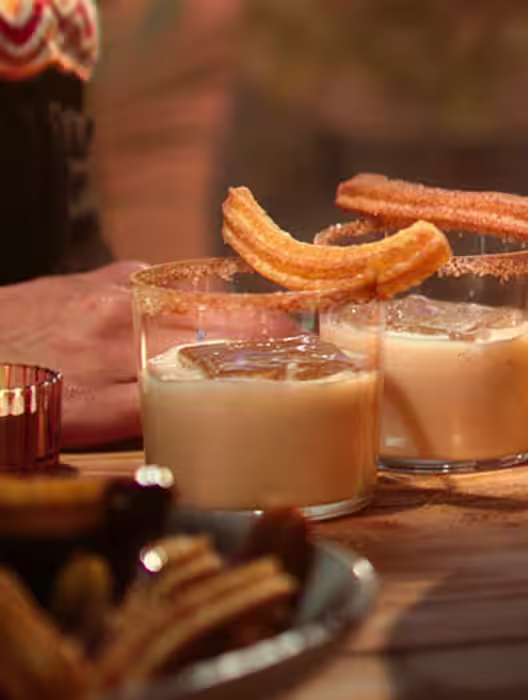 At an outdoor party, there's people with a tasty Irish Cactus cocktail- made of Baileys and tequila, topped with sugary churros.