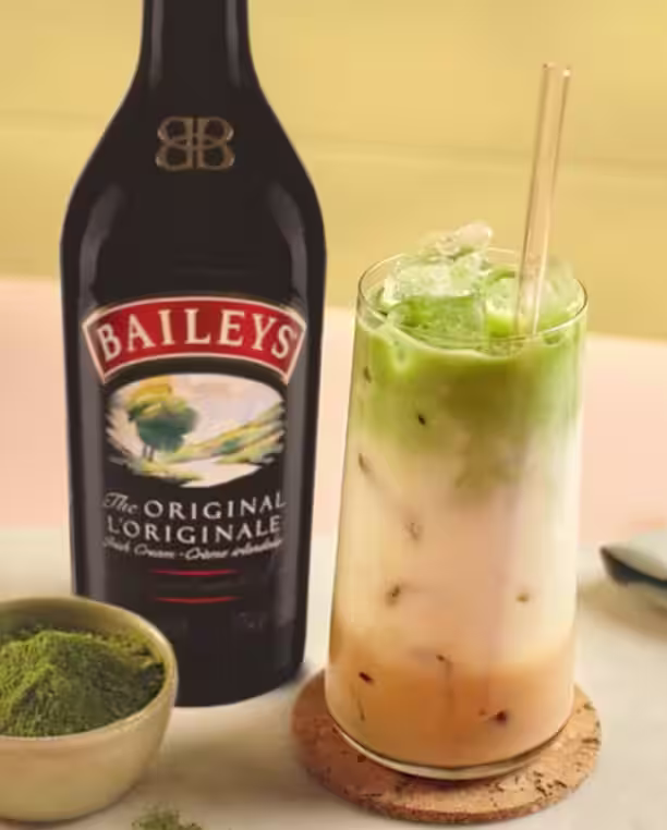 Un verre de Baileys Matcha Latte à côté d'une bouteille de Baileys Original Irish Cream.